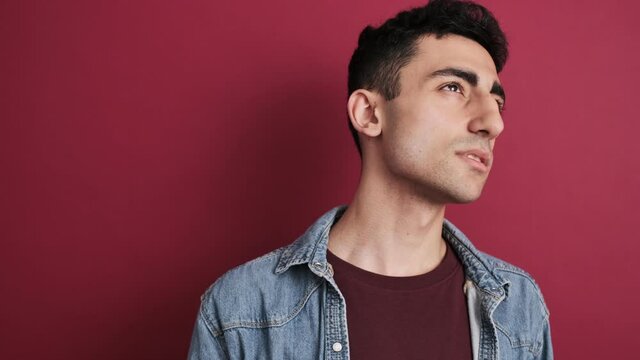 A thinking brunette man is looking to the side standing isolated over red background in the studio