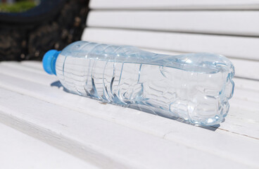 Plastic bottle of pure water left on a white wooden bench on a sunny summer day. Thirst in the hot...