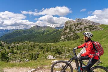 pretty active senior woman riding her electric mountain bike up to Valparola Pass in the Alta Badia Dolomites , South Tirol and Trentino, Italy