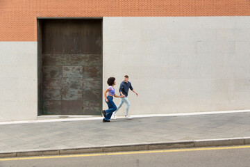 young multiracial man and woman running and talking in the city with a wall in the background with copy space