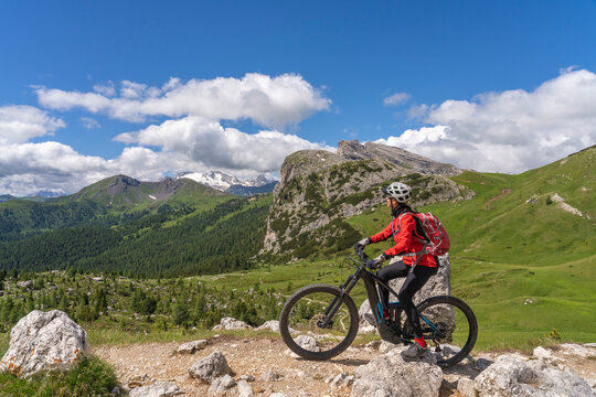 pretty active senior woman riding her electric mountain bike up to Valparola Pass in the Alta Badia Dolomites , South Tirol and Trentino, Italy © Uwe