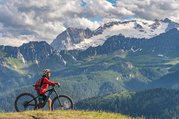 Fototapeta premium nice and active senior woman riding her electric mountain bike on the Pralongia Plateau in the Alta Badia Dolomites with glacier of Marmolata summit in Background, South Tirol and Trentino, Italy 