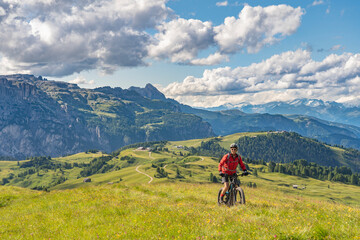 Fototapeta na wymiar nice and active senior woman riding her electric mountain bike on the Pralongia Plateau in the Alta Badia Dolomites with mountains of Sella Group in Background, South Tirol and Trentino, Italy