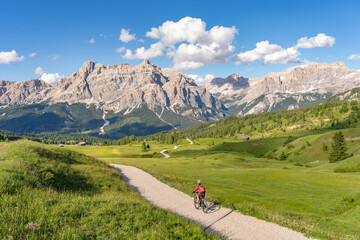 Fototapeta na wymiar nice and active senior woman riding her electric mountain bike on the Pralongia Plateau in the Alta Badia Dolomites with awesome Sasso die Santa Cruce summit in Backg, South Tirol and Trentino, Italy