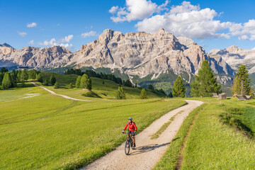 Obraz premium nice and active senior woman riding her electric mountain bike on the Pralongia Plateau in the Alta Badia Dolomites with awesome Sasso die Santa Cruce summit in Backg, South Tirol and Trentino, Italy