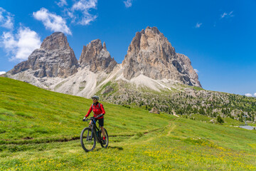 pretty beautiful senior woman riding her electric mountain bike below famous Sassolungo summit in...