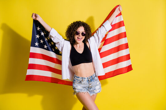 Photo of impressed excited young lady wear white shirt glasses holding american flag isolated yellow color background