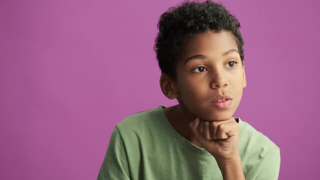 A thinking little boy is looking to the side isolated over purple background in the studio