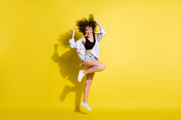 Photo of funny lucky young lady wear black top smiling jumping rising fists isolated yellow color background