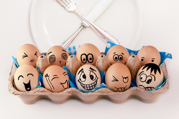 Easter eggs with different faces in eggbox and round plate with cutlery, knife and fork. Types of...