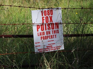 1080 fox poison bait laid on this property sign attached to rusted barbed wire fence with tall...