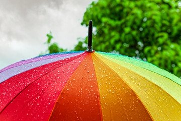 Rain On Rainbow Umbrella. Umbrella under heavy rain against cloudy sky background. Rainy weather...