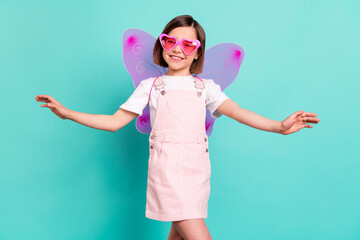 Photo of adorable cute school girl wear pink overall glasses wings smiling dancing isolated teal...