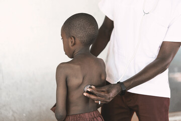African ethnicity black male doctor checking respiratory health conditions of a little African boy...