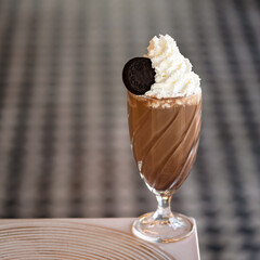 Refreshing drink. Glass of chocolate milkshake cocktail with Airy foam or froth and cookie on top. Puffy whipped cream dessert on blurred background. Soft focus. Soft focus. Copy space at left.