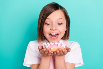 Photo of pretty hungry school girl wear pink overall smiling eating tasty doughnut isolated teal color background