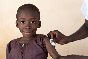 Healthcare professional cleaning the injection site on the arm of a smiling little African boy