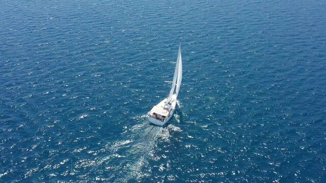 White sailboat on the sea. Leisure sailing on blue lake or ocean during summer vacation in the Mediterranean. Drone circling around a wind propelled yacht - aerial view: adventure, recreation, luxury.
