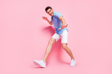 Fototapeta na wymiar Photo of funky positive guy walk having fun wear blue shirt shorts sneakers isolated on pink color background