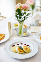 Three cheesecakes on a white plate with jam, on the table against the background of a vase with flowers, restaurant
