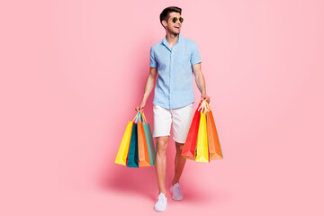 Photo of man walk carry store bags look empty space wear sunglass blue shirt isolated on pink color...