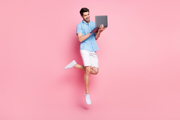 Full length body size photo man working on laptop jumping in summer isolated pastel pink color background