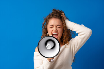 Young smiling expressive caucasian woman shout in megaphone against blue background