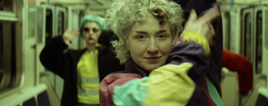 Anamorphic Shot Of Young Caucasian Female Dancer In Trendy Vintage Jacket Looking At Camera And Dancing Vogue While Standing In Front Of Dance Crew In Subway Train