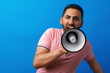 Young arab man with megaphone proclaiming something isolated on blue background