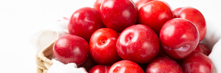 Chinese or Korean red plum in a basket on a white table closeup. Summer harvest. Banner