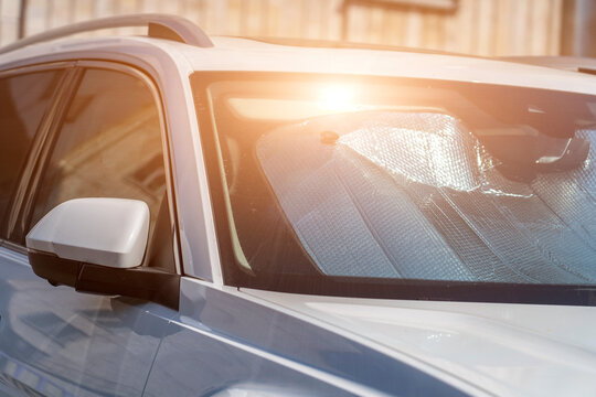 Sun visor or sun reflector on car windshield protects car in parking lot. There is light from sun shining on windshield