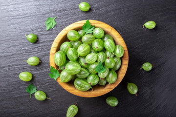 Fresh gooseberries in wooden bowl on black stone slate background.