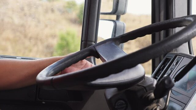 Lorry driver riding to destination at country road. Male hand of trucker holds a big steering wheel while operating a truck through countryside. Concept of logistics and transportation. Close up