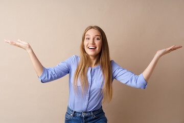 Surprised young blonde woman throwing up her hands against beige background