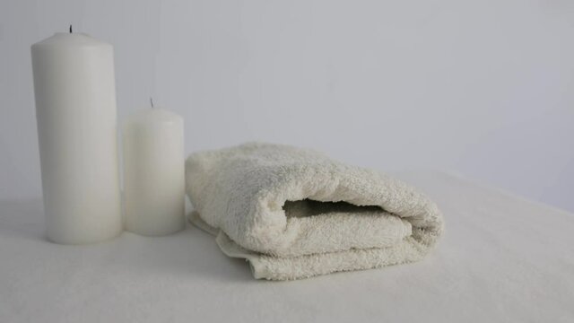 A moving focus on white candles and a folded towel in a white environment