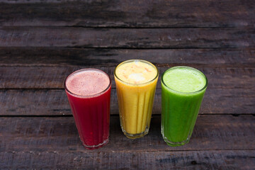 three glasses of red yellow and green natural juices on wooden background.