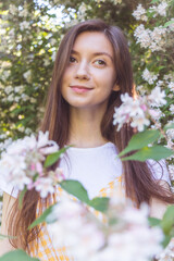 Fototapeta premium Portrait of a beautiful brunette girl in a white t-shirt among flowering weigela branches