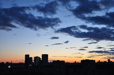 Dark city buildings at dusk and dramatic clouds hanging over them.
