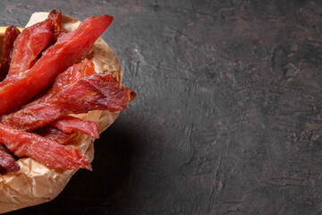 Jerky meat strips with spices and herbs on a paper on a dark background. Tipical Italian food coppiette is a spiced pork meat strips. Snacks for beer, top view, copy space