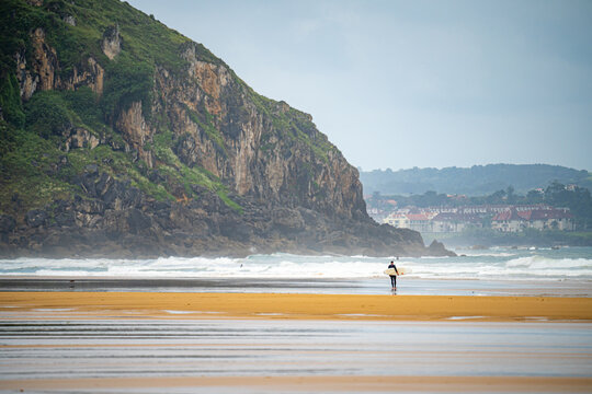 People walking with surfboards and surfing, in the city of Somo in the province of Santander, Spain, near large cliffs and virgin beaches
