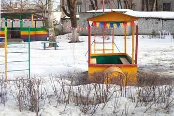 On the playground in winter you can see the stairs, an iron house-locomotive, a veranda and above them bright multi-colored flags