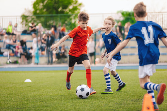 Group of boys in two kids soccer teams competing for the ball on a football tournament match. Soccer school children playing game on grass pitch. Football stadium full of fans in background
