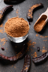 Dry carob pods and carob powder over dark background