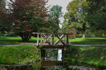 Small wooden bridge over still water with large stones surrounded by trees and fresh grass