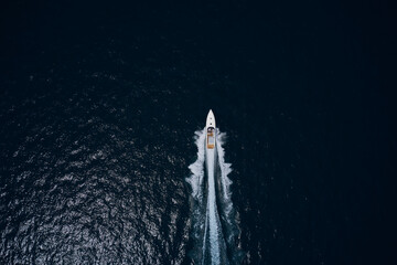 Large white boat driving on dark water. Speedboat on dark blue water aerial view. Speedboat wave speed water. Speed boat faster movement on the water top view. Speedboat movement on the water.