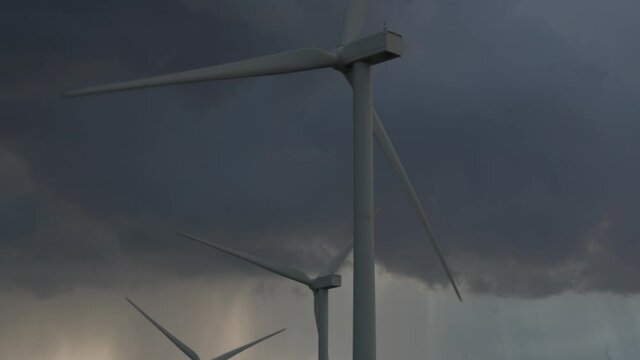Renewable energy generator windmills with large blade silhouettes rotate on wind farm under dense storm clouds in evening. Sustainable clean energy concept.