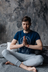 A young man sitting in meditation with his hands folded in a yoga mudra