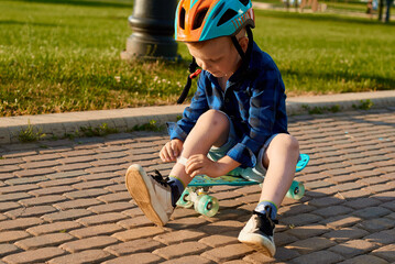 A small five-year-old boy in a helmet fell off a skateboard, injured his leg and is sealing it with a plaster © Hanna