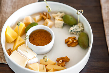 A plate with cheese, honey, olives and nuts is on the table.