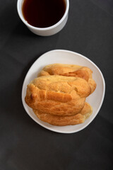 Eclairs on plate and cup of tea top view. Profiteroles on saucer on gray background. Baking for tea